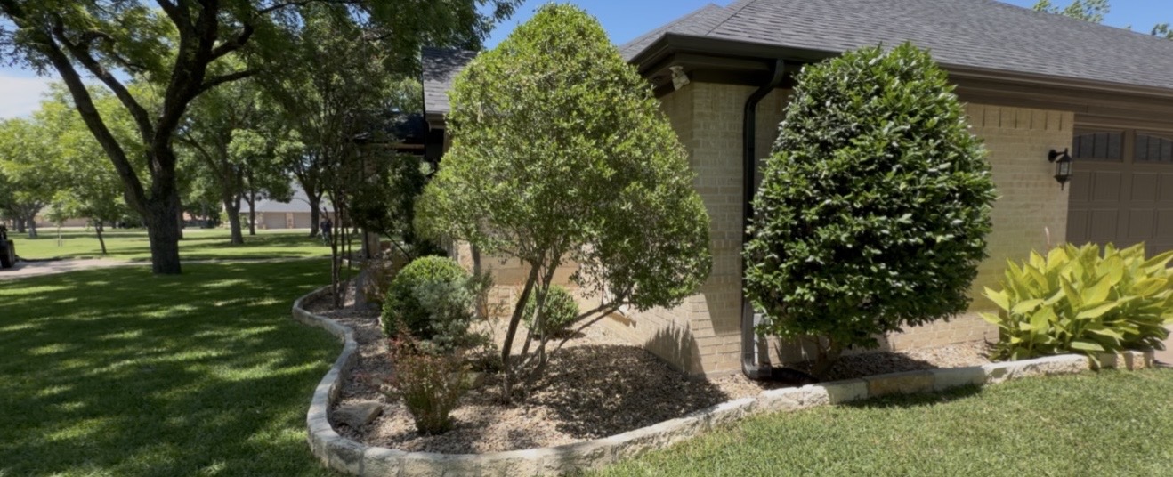 Curved stone border landscape bed with trimmed shrubs and trees